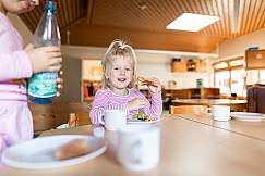 Mädchen sitzt am Essenstisch und lächelt in die Kamera
