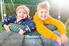 Zwei Kinder liegen in der Nestschaukel